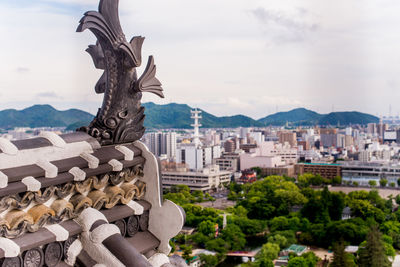 Statue of buildings in city against cloudy sky