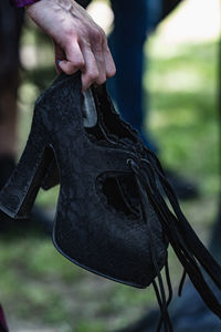 Close-up of man holding shoes hanging outdoors