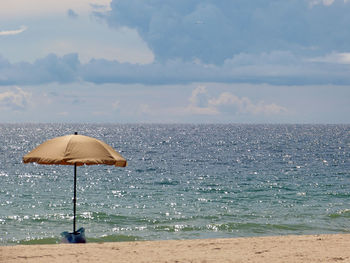 Umbrella at beach against cloudy sky on sunny day