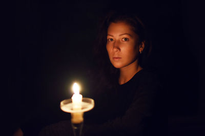 Portrait of woman against illuminated candle in darkroom