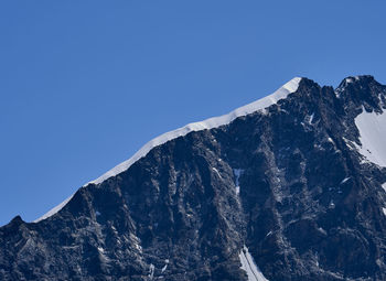 Low angle view of snowcapped mountains ridge against clear blue sky