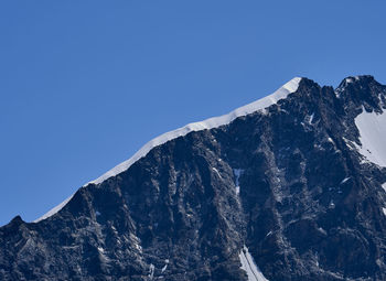 Low angle view of snowcapped mountains against clear blue sky