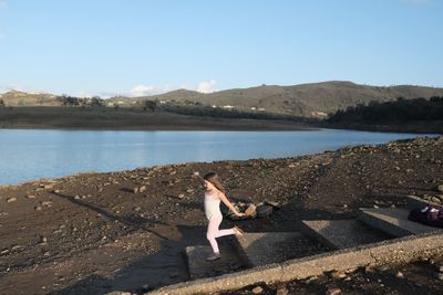 Girl dancing on shore by lake against sky