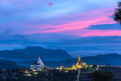 Illuminated buildings in city against sky at sunset