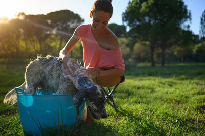 Middle-aged woman bathing her dog in the garden on a sunny day surrounded by trees.