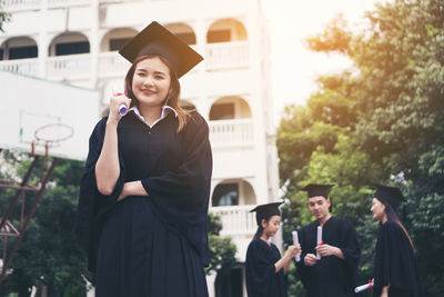 Cheerful student in graduation gown standing outdoors