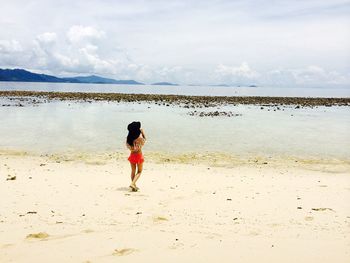 Rear view of woman walking on beach against sky