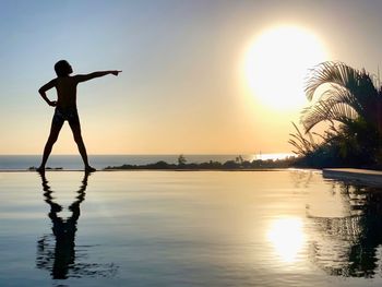 Silhouette person standing by swimming pool against sky during sunset