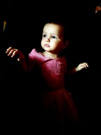 Cute boy looking away while standing against black background