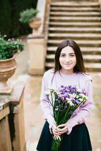 Portrait of beautiful woman holding colorful flowers while standing against steps