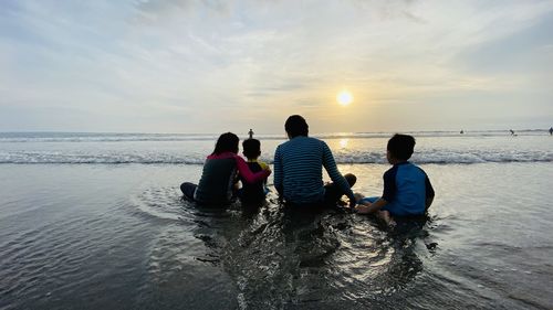 Rear view of women on sea against sky during sunset