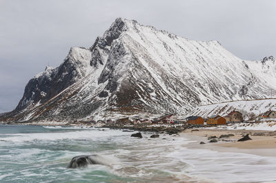 Buildings near ocean in front of snow covered mountain