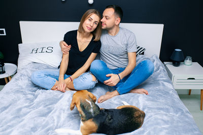 Portrait of couple sitting on bed with dog