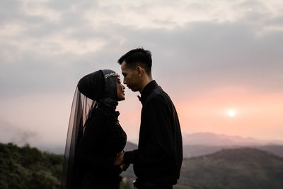 Side view of young man standing against sky during sunset