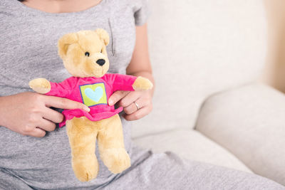 Midsection of woman holding teddy bear while sitting on sofa at home