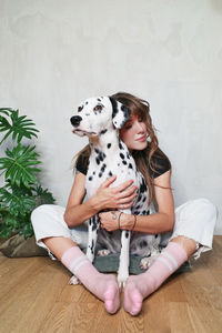 Woman with dog sitting on hardwood floor against wall at home