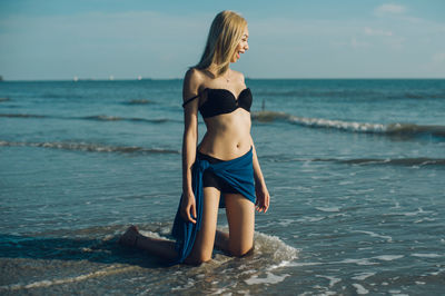 Beautiful smiling fashion model kneeling at beach