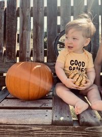 Cute smiling boy sitting by pumpkin outdoors