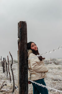 Side view of young woman standing on wooden post