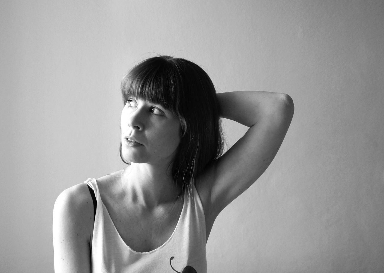 Thoughtful young woman with hand behind head against wall