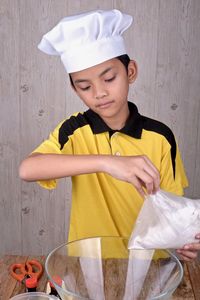 Boy wearing chef hat preparing food in kitchen at home