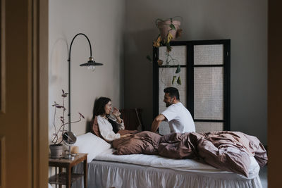 Couple talking to each other while sitting on bed at home