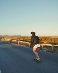 Woman skateboarding on road against blue sky