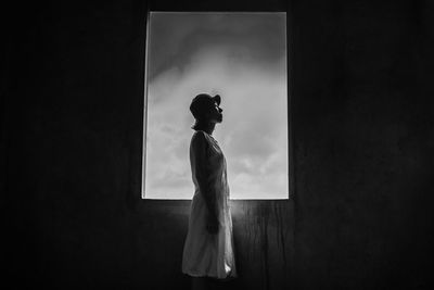 Side view of young woman standing by window in darkroom