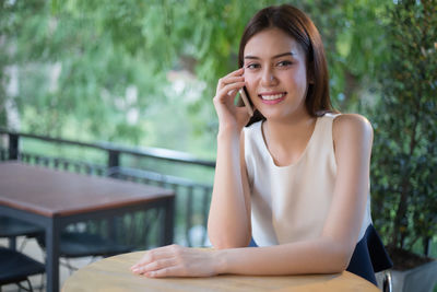 Portrait of smiling young woman using phone while sitting at sidewalk cafe