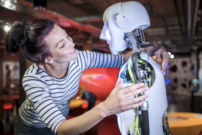 Smiling technician with arm around human robot at workshop