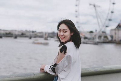 Portrait of smiling young woman standing against water