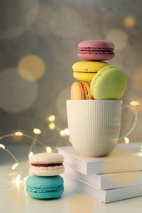White coffee cup filled with macaroons on the table, fairy lights and bokeh background