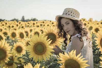 Close-up portrait of young woman standing against sunflower field