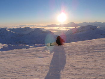 People on snow covered landscape against sky during sunset