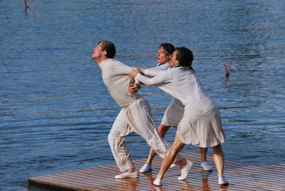 Women catching man hands while standing on pier against sea