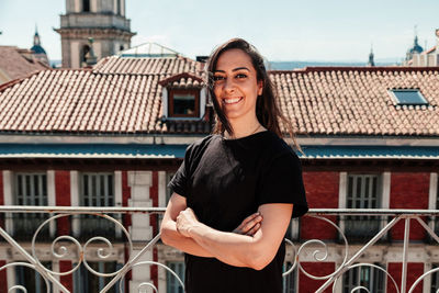 Portrait of smiling young woman standing against building in city