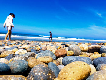 Full length of man standing on rocks at beach against blue sky