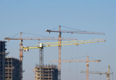 Cranes at construction site against clear blue sky