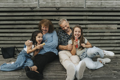 Full length of happy grandparents and granddaughters sitting on floorboard