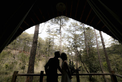 Rear view of couple walking on bridge in forest