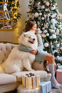 Little cute girl sitting on the sofa with samoyed dog