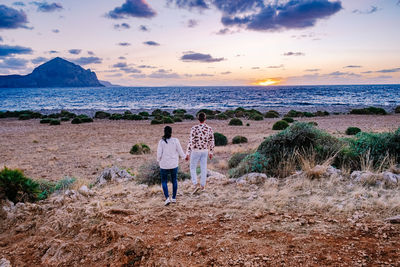 Rear view of people on beach against sky during sunset