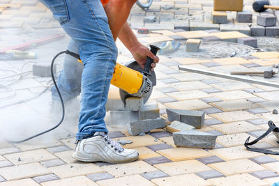 A worker cuts stone tiles while laying them on a sidewalk.