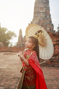 An asian girl in thai traditional dress holding an umbrella in wat chai wattanaram in ayutthaya