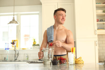 Shirtless teenage boy preparing juice in kitchen at home