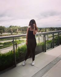 Full length of young woman standing on railing against bridge