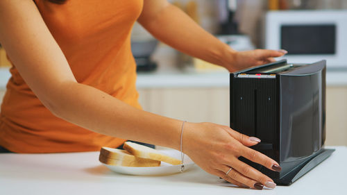 Midsection of woman using toaster at home