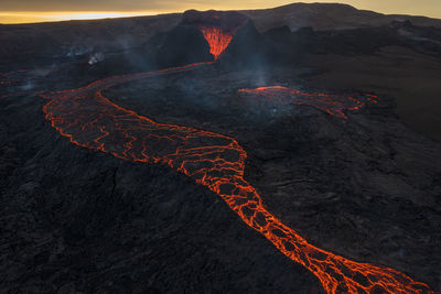 Drone view of stream of hot orange lava flowing through mountainous terrain in morning in iceland