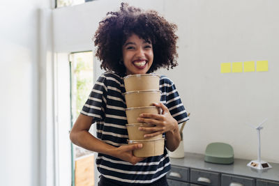 Happy businesswoman holding lunch boxes in office