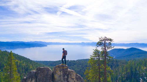 Rear view of man standing on rock against the lake and sky